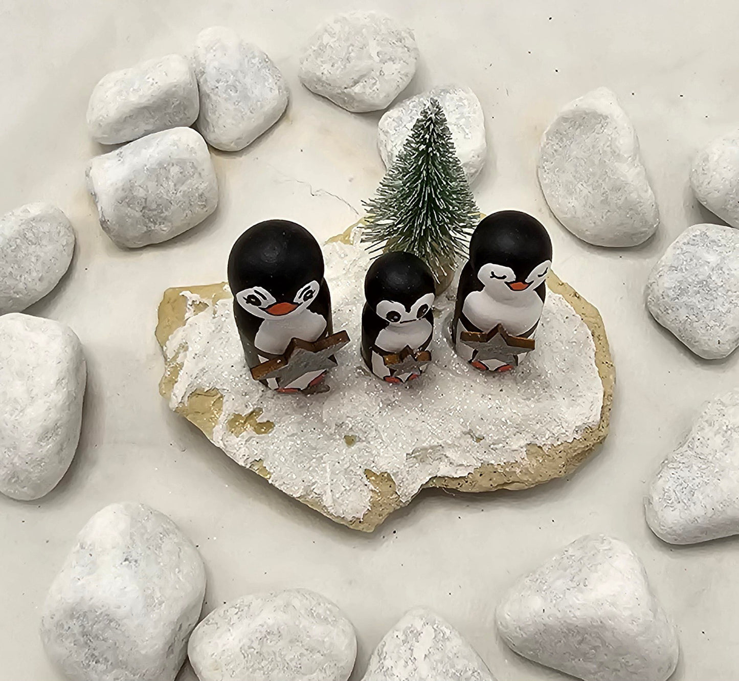 Pinguine Miniatur, gefertigt aus  kleinen Holzkegeln, auf Sandstein mit Bäumchen.