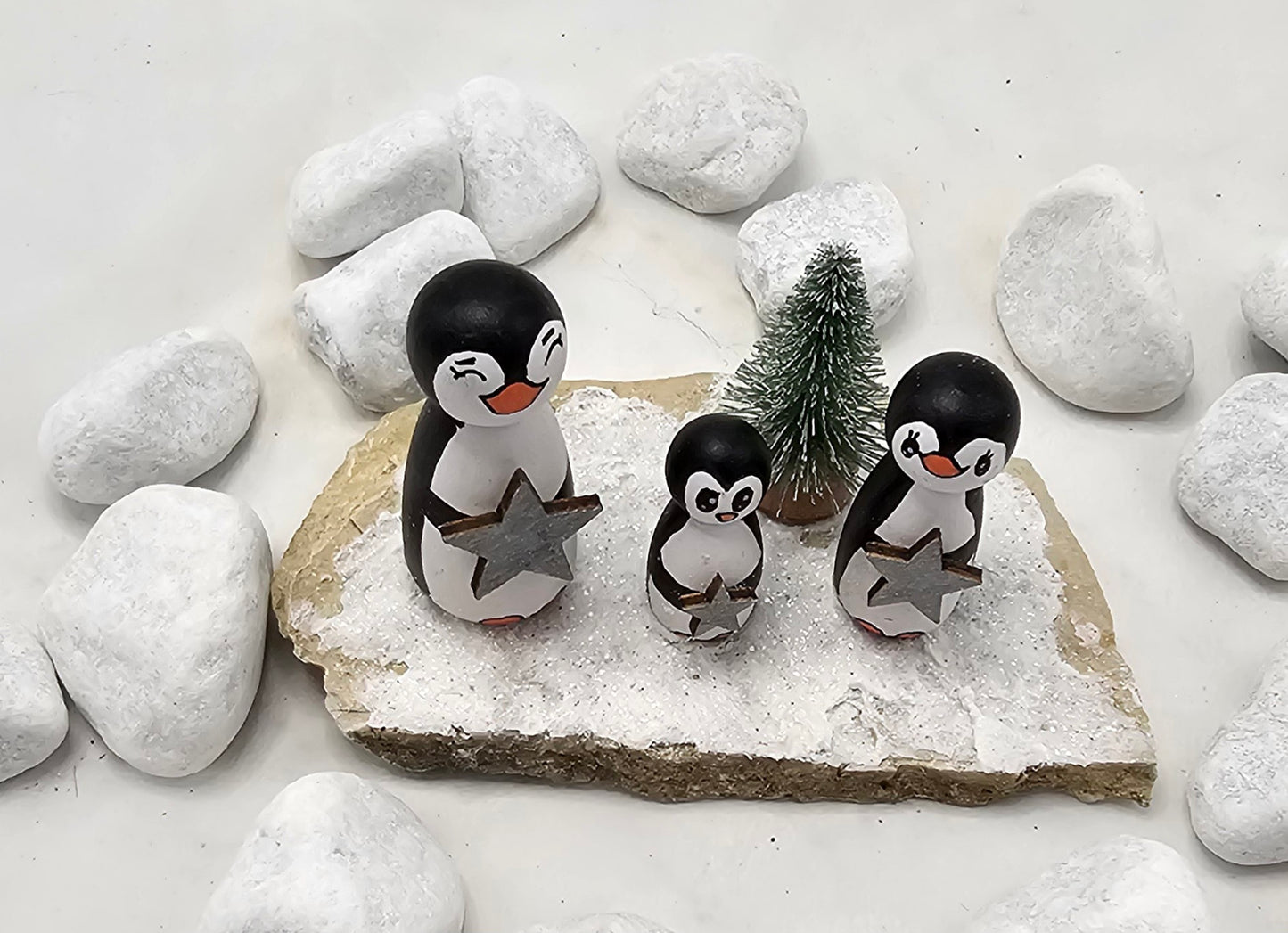 Pinguine Miniatur, gefertigt aus  kleinen Holzkegeln, auf Sandstein mit Bäumchen.