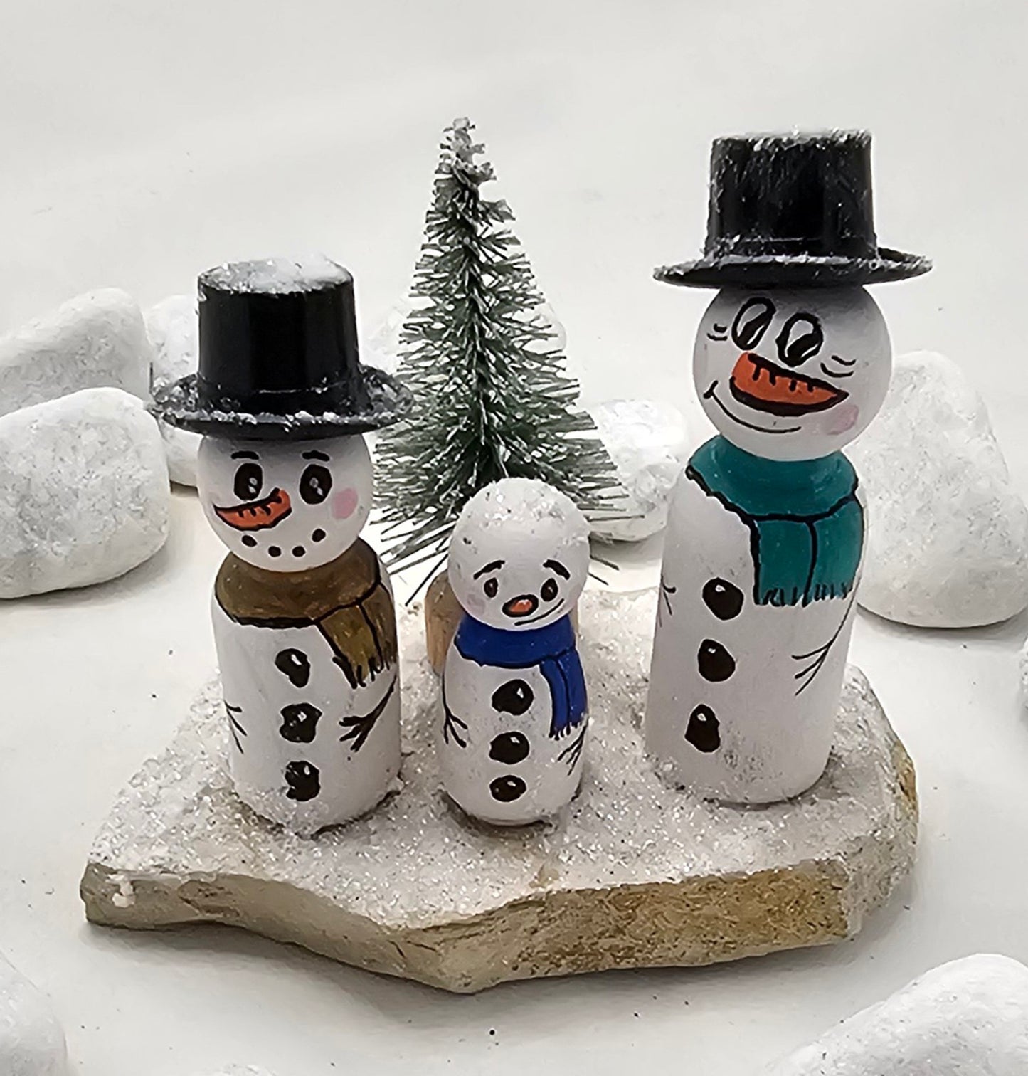 Schneemänner Miniatur, gefertigt aus  kleinen Holzkegeln, auf Sandstein mit Bäumchen.