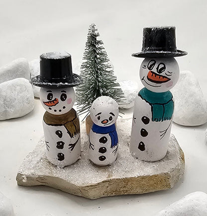 Schneemänner Miniatur, gefertigt aus  kleinen Holzkegeln, auf Sandstein mit Bäumchen.