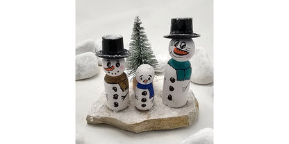 Schneemänner Miniatur, gefertigt aus  kleinen Holzkegeln, auf Sandstein mit Bäumchen.