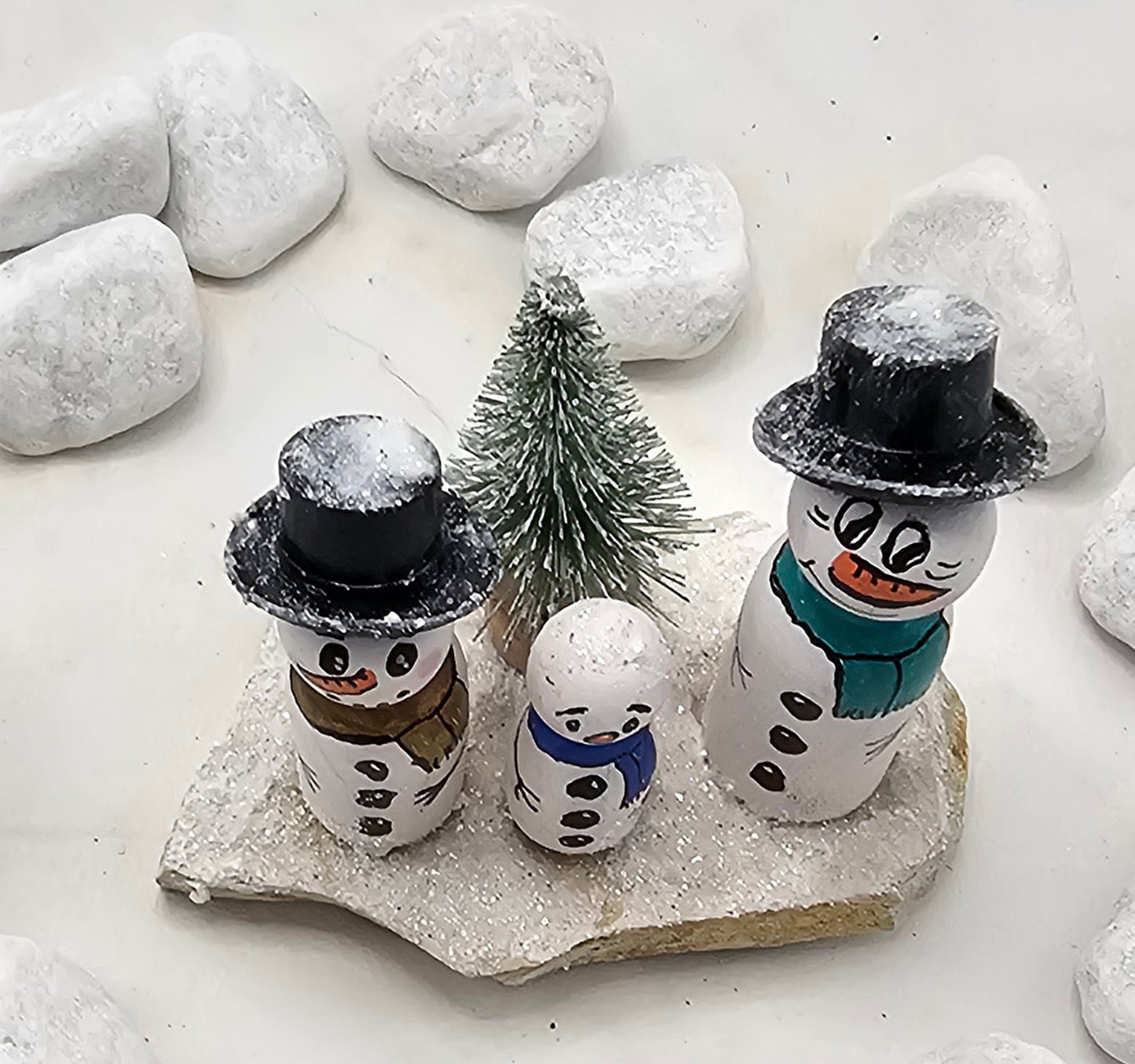 Schneemänner Miniatur, gefertigt aus  kleinen Holzkegeln, auf Sandstein mit Bäumchen.