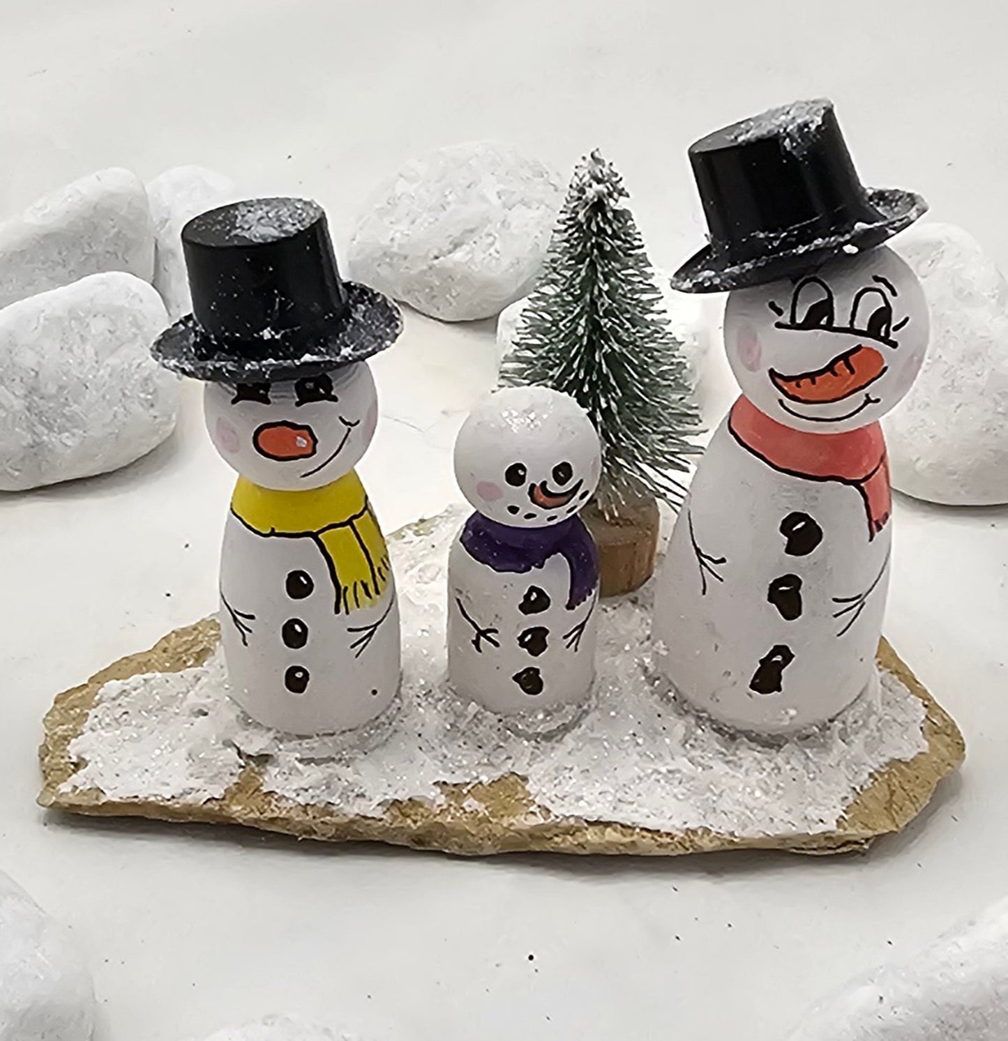 Schneemänner Miniatur, gefertigt aus  kleinen Holzkegeln, auf Sandstein mit Bäumchen.