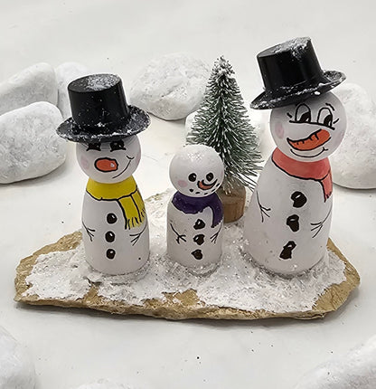 Schneemänner Miniatur, gefertigt aus  kleinen Holzkegeln, auf Sandstein mit Bäumchen.